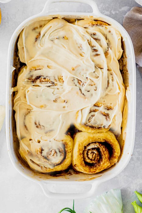 Top view of frosted dairy free pumpkin cinnamon roll dough in a white baking dish