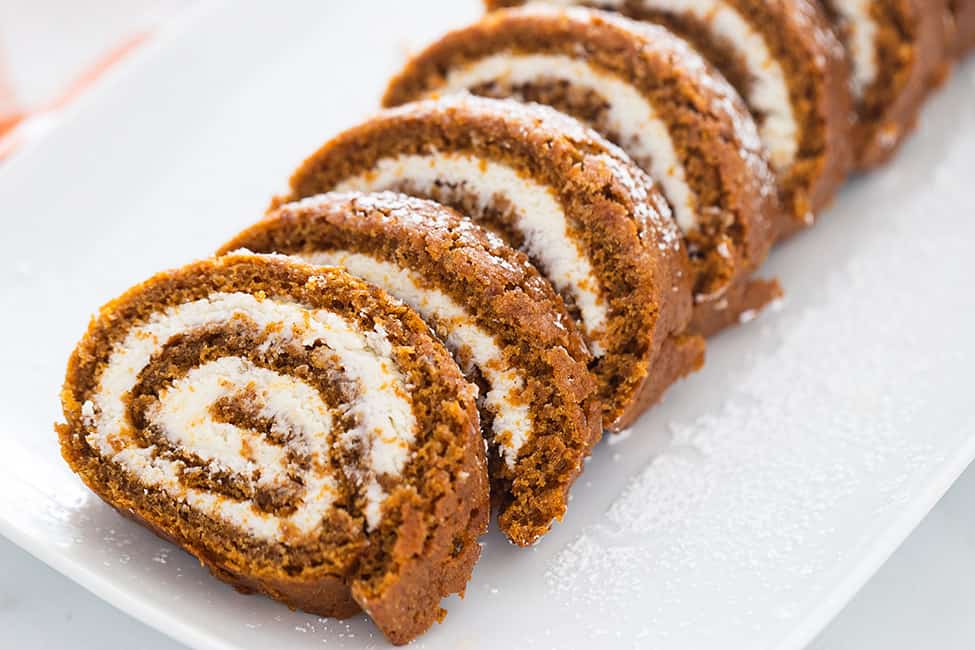 Sliced pumpkin roll on a serving platter with powdered sugar