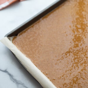 Pumpkin spice roll cake batter in a parchment-lined sheet pan