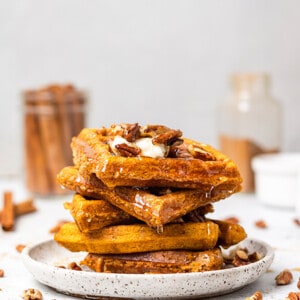 A stack of 5 gluten free pumpkin waffles with chopped pecans and maple syrup