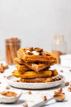 A stack of 5 gluten free pumpkin waffles with chopped pecans and maple syrup