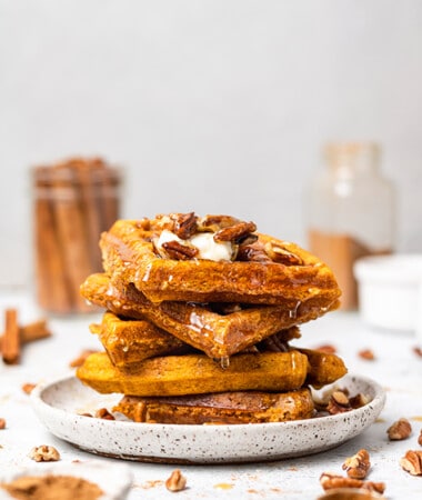 A stack of 5 gluten free pumpkin waffles with chopped pecans and maple syrup