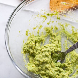 Mashed avocado with a fork in a clear mixing bowl
