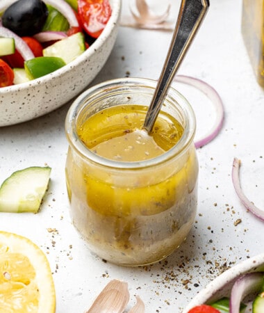 45 degree shot of greek salad vinaigrette in a small jar with a spoon