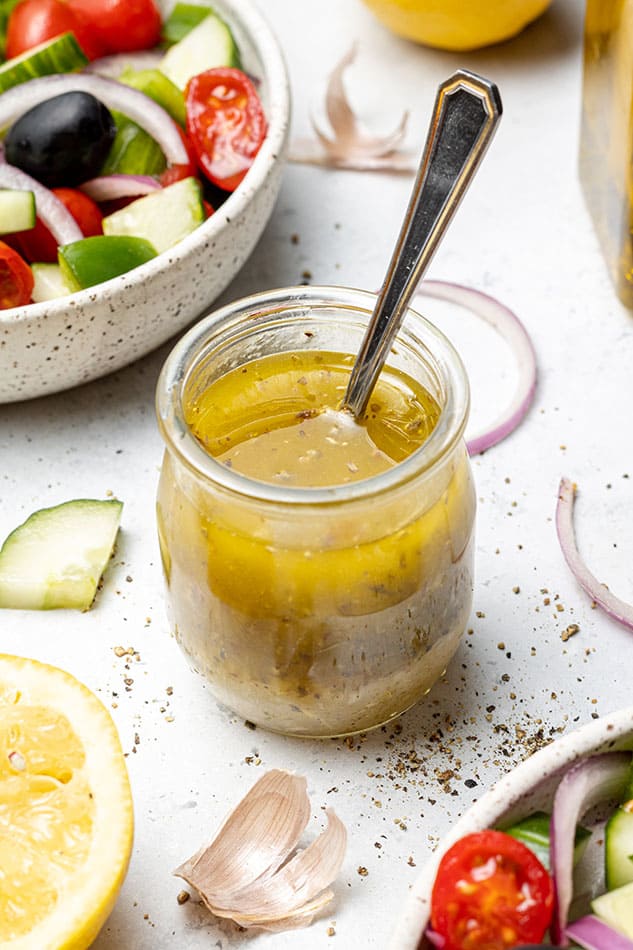 45 degree shot of greek salad vinaigrette in a small jar with a spoon