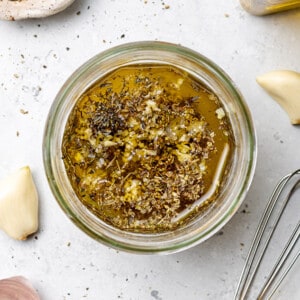 Top view of ingredients to make greek salad dressing (lemon juice, vinegar, oil, garlic and dried herbs) in a glass jar