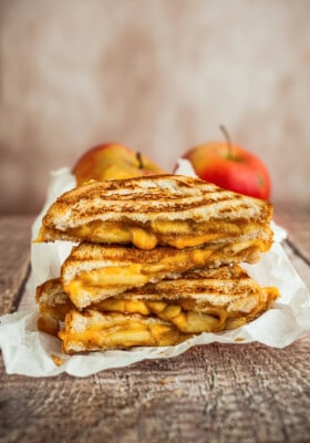 Side shot of grilled cheese sandwich halves stacked on top of white parchment paper