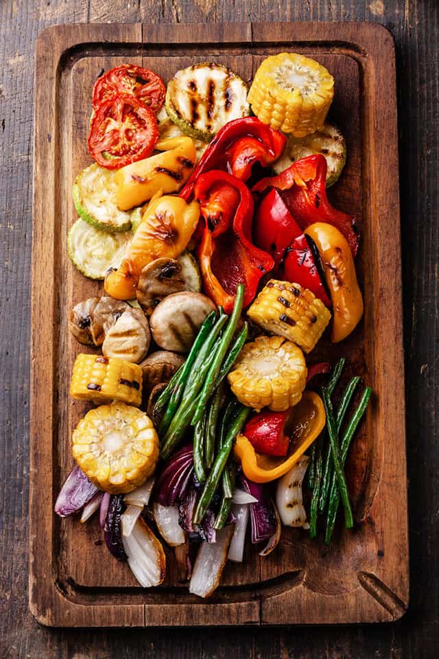 Grilled vegetables on cutting board on dark wooden background