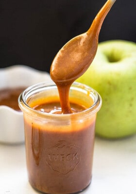 Side shot of a jar full of easy caramel sauce with a spoonful