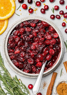 Overhead view of homemade cranberry sauce in a bowl with fresh herbs and spices nearby