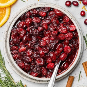 Overhead view of homemade cranberry sauce in a bowl with fresh herbs and spices nearby