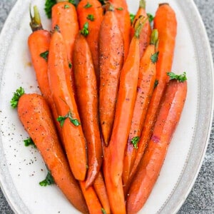 A pile of honey roasted carrots with parsley on a white oval platter