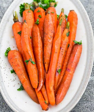 A pile of honey roasted carrots with parsley on a white oval platter