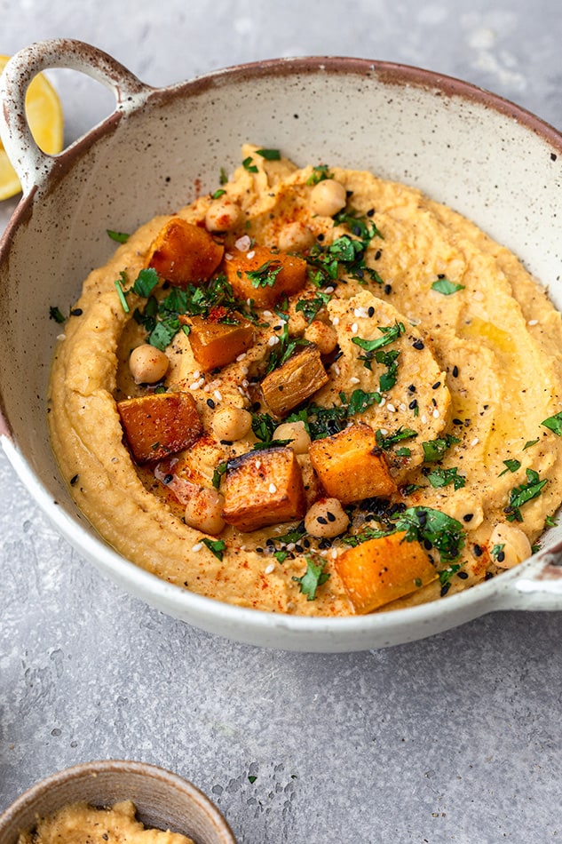 Sweet potato hummus in a dish topped with chunks of sweet potato, chickpeas and fresh herbs