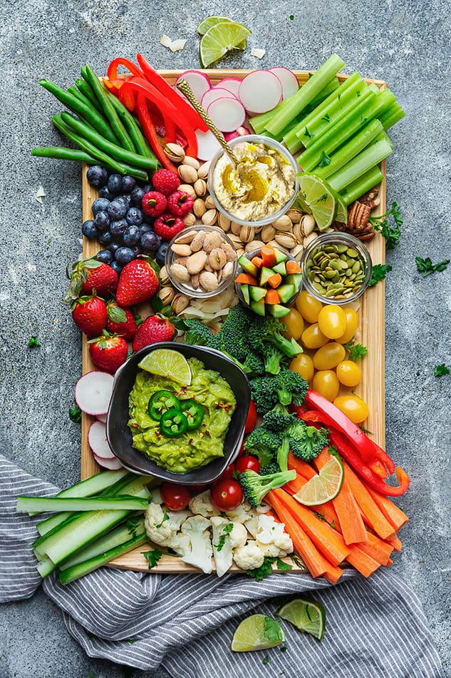 Overhead view of a veggie and fruit board with dipping sauces and nuts