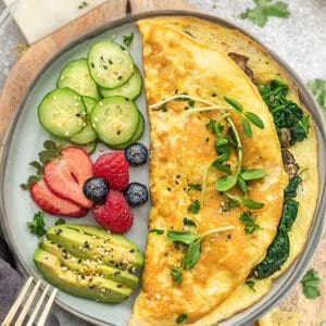 Top view of easy omelette with avocado, berries and cucumber on a grey plate on a a grey background with a gold fork