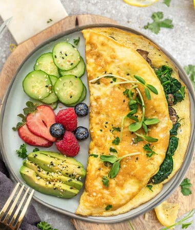 Top view of easy omelette with avocado, berries and cucumber on a grey plate on a a grey background with a gold fork