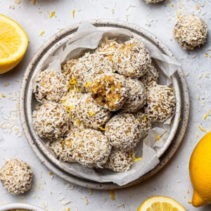 Overhead view of a pile of lemon bliss balls one with a bite taken in a white bowl