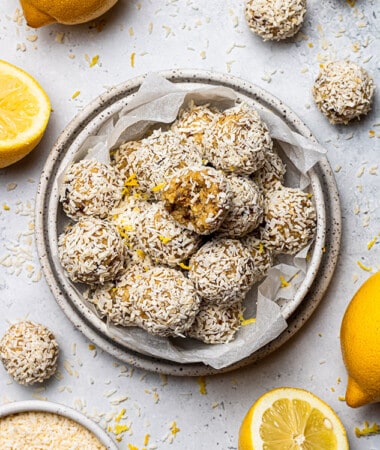 Overhead view of a pile of lemon bliss balls one with a bite taken in a white bowl