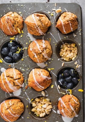Eight Glazed Lemon Poppy Seed Muffins in a muffin pan with blueberries