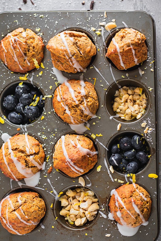 Overhead view of Lemon Poppyseed Muffins in a tin drizzled with icing and garnished with blueberries and chopped nuts