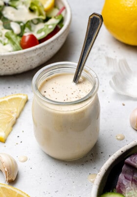 45 degree shot of lemon tahinin dressing in a small jar with a spoon