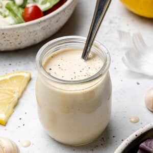 45 degree shot of lemon tahinin dressing in a small jar with a spoon