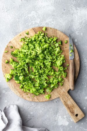 Top view of finely chopped broccoli on a wooden cutting board