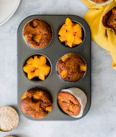 Overhead view of a muffin tin with paleo peach muffins and diced peaches