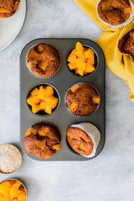 Overhead view of a muffin tin with paleo peach muffins and diced peaches