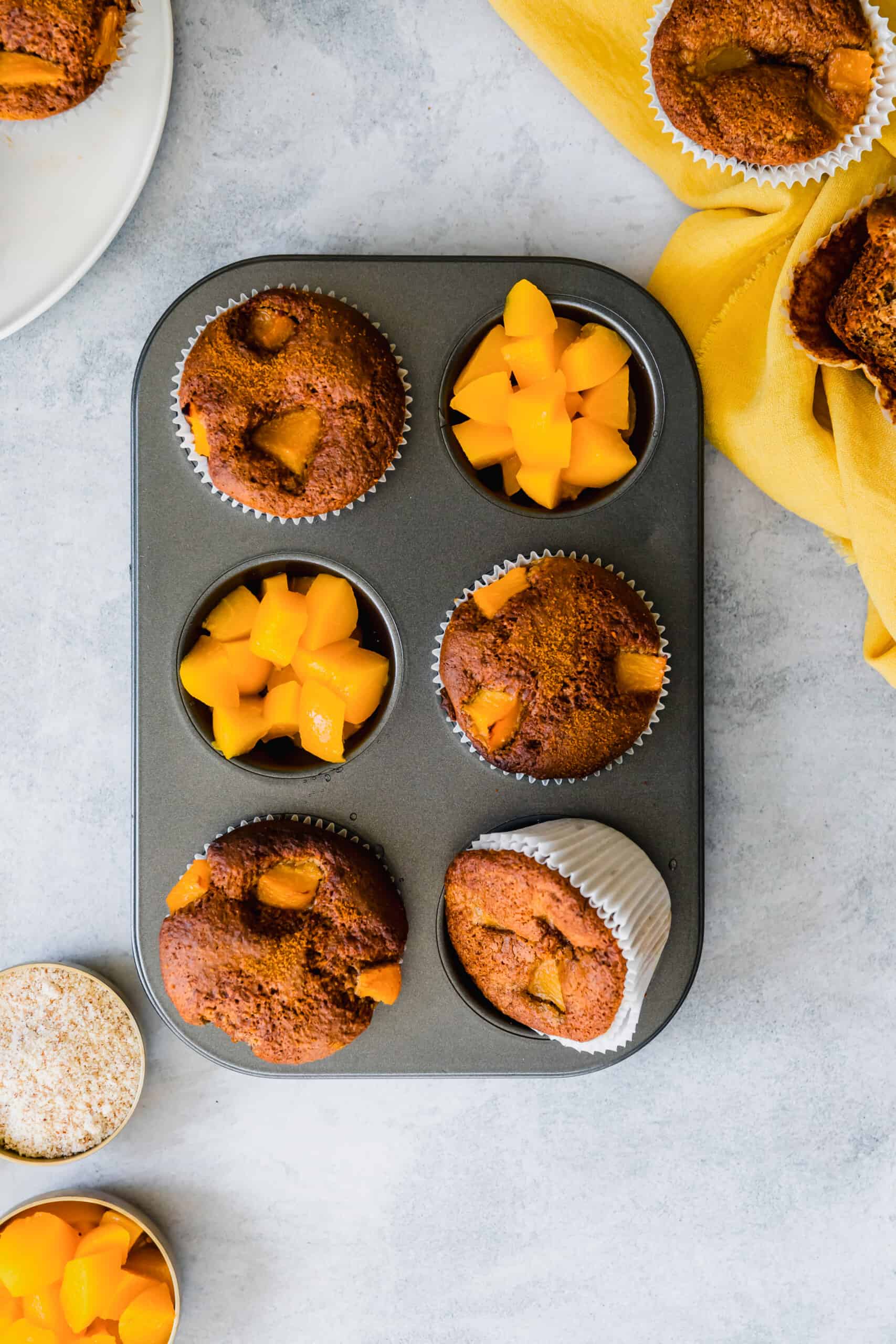 Overhead view of a muffin tin with peach muffins and diced peaches