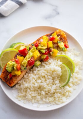 Overhead shot of one serving of mango salsa salmon on a white plate with a side of cauliflower rice with lime