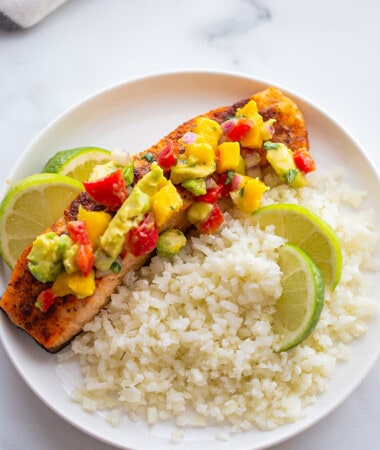 Overhead shot of one serving of mango salsa salmon on a white plate with a side of cauliflower rice with lime