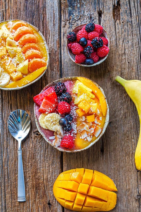 Top view of an easy mango smoothie recipe in a white bowl topped with fresh berries and a spoon