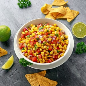 A serving of summer corn salad in a white bowl with tortilla chips on the side