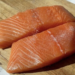 Two raw salmon fillets on a wooden cutting board