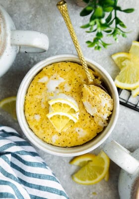 Top view of lemon mug cake in a white mug on a grey background with a gold spoon