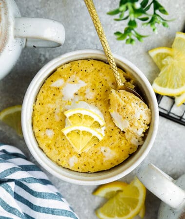 Top view of lemon mug cake in a white mug on a grey background with a gold spoon