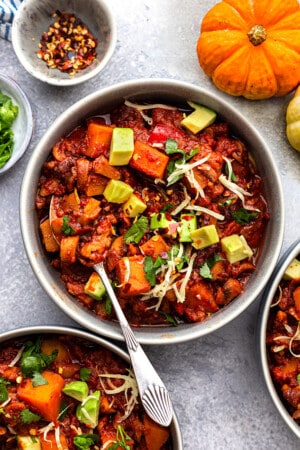 Top view of Pumpkin Chili in a white bowl with a spoon on a grey background