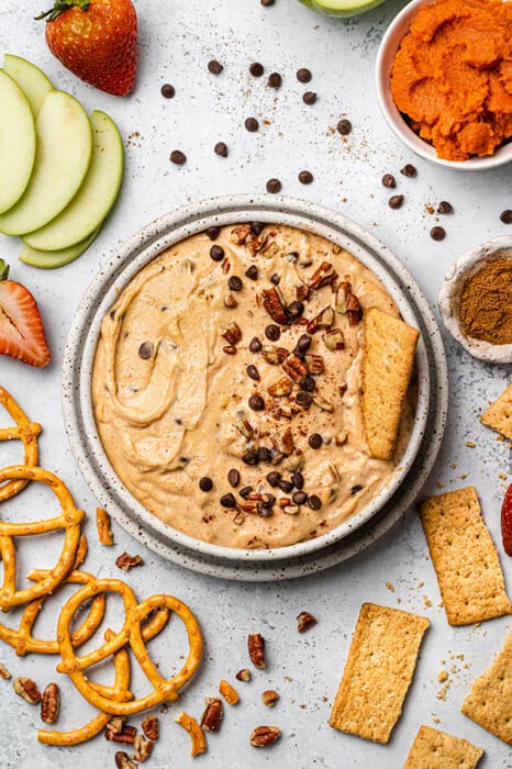 Overhead view of pumpkin dip in a bowl with mini chocolate chips, chopped nuts, and a cracker