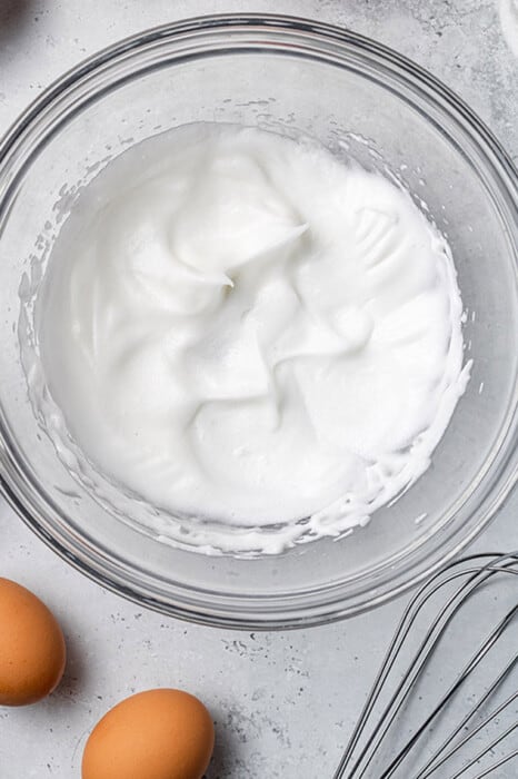 Whipped egg whites beaten until stiff peaks in a clear mixing bowl.