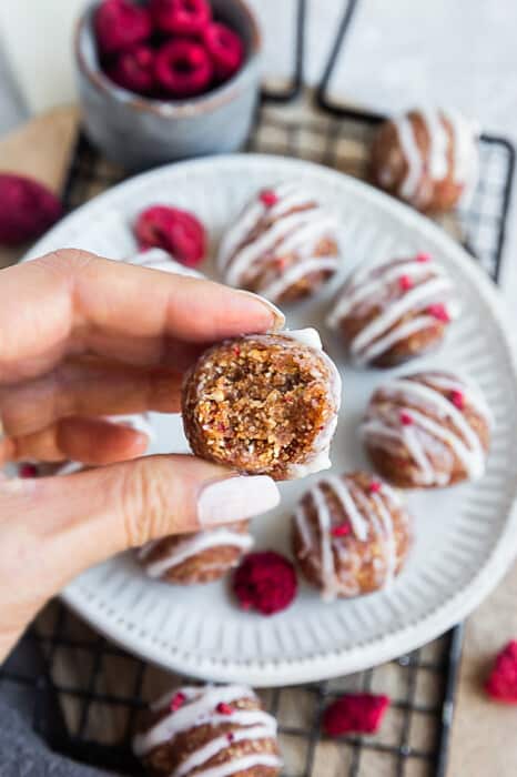 Hand holding one easy raspberry protein ball with a missing bite