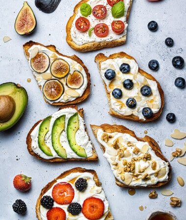 Six pieces of ricotta toast with various toppings on a gray countertop