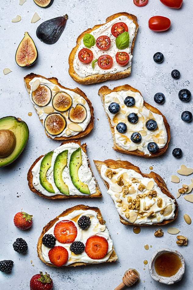 Six pieces of ricotta toast with various toppings on a gray countertop