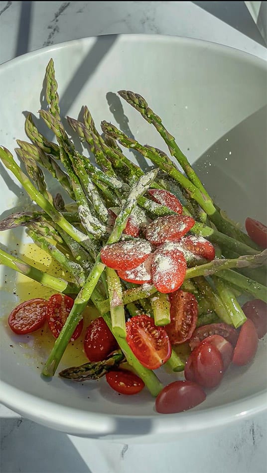 Overhead view of asparagus and cherry tomatoes in a bowl with oil and seasonings