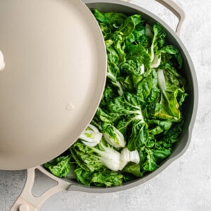 A pile of uncooked bok choy in a large wok with the lid