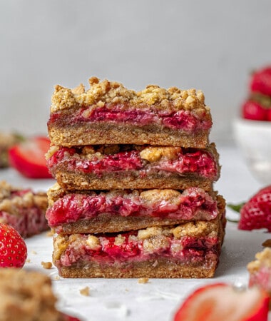 Side view of four strawberry oat crumb bars stacked on a white background