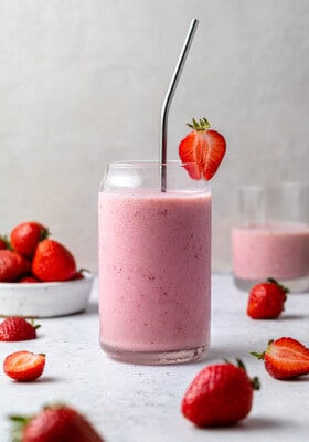 A strawberry smoothie in a glass with a metal straw and a strawberry garnish