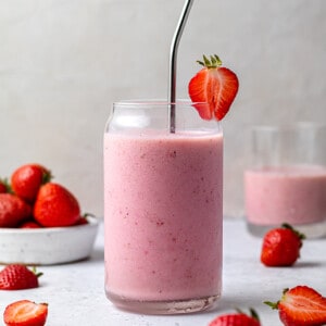 A strawberry smoothie in a glass with a metal straw and a strawberry garnish