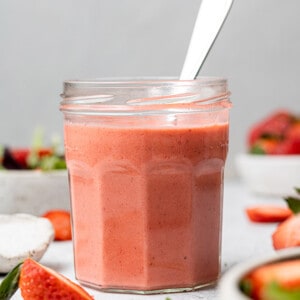 Side view of strawberry vinaigrette dressing in a small jar with a spoon